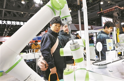 2025上海国际机床展上，参观者在一个进行作业演示的双臂协同机器人前驻足观看。  新华社记者 方喆摄